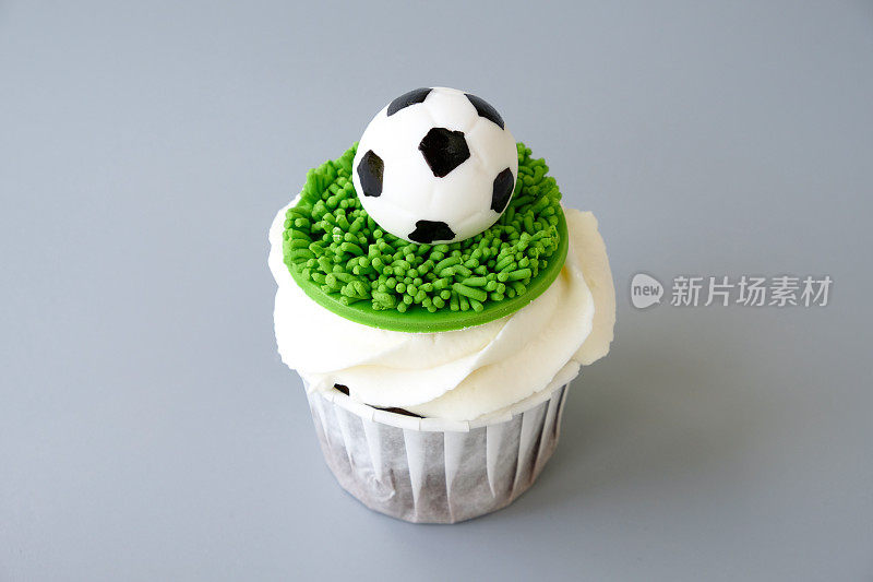 以足球为主题的巧克力小蛋糕，白色的奶油装饰着绿草，灰色的背景是足球。