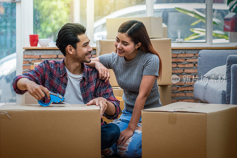 亚洲年轻夫妇正在打包大纸板箱准备搬新家，搬家和找房子的概念，