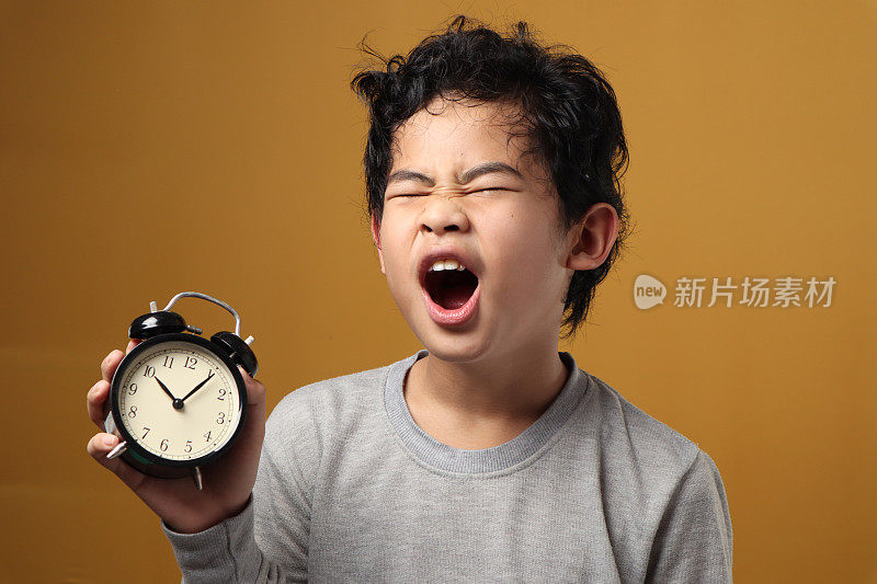 亚洲男孩拿着闹钟打哈欠，瞌睡累了的小孩，晚醒了
