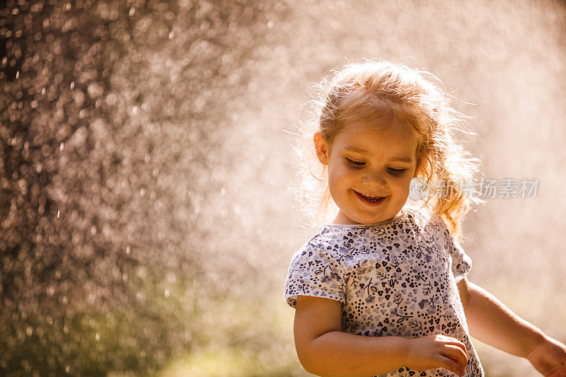 快乐的小女孩在室外跳舞，花园里的水管在浇草