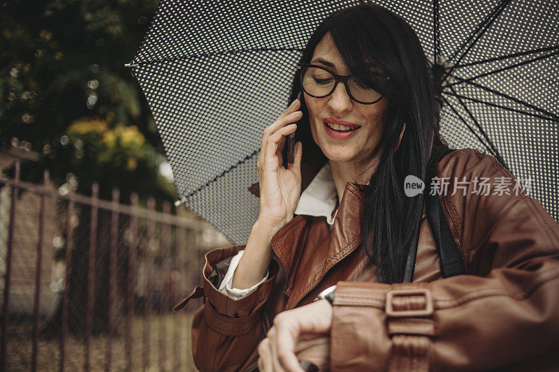 一位漂亮的商务老妇人在雨中行走，手里拿着手机