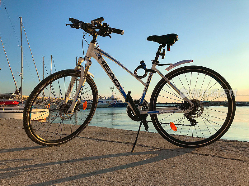 HEAD公司的蓝白相间的自行车停在海边。日落时分，保加利亚布尔加斯附近的萨拉佛渔港