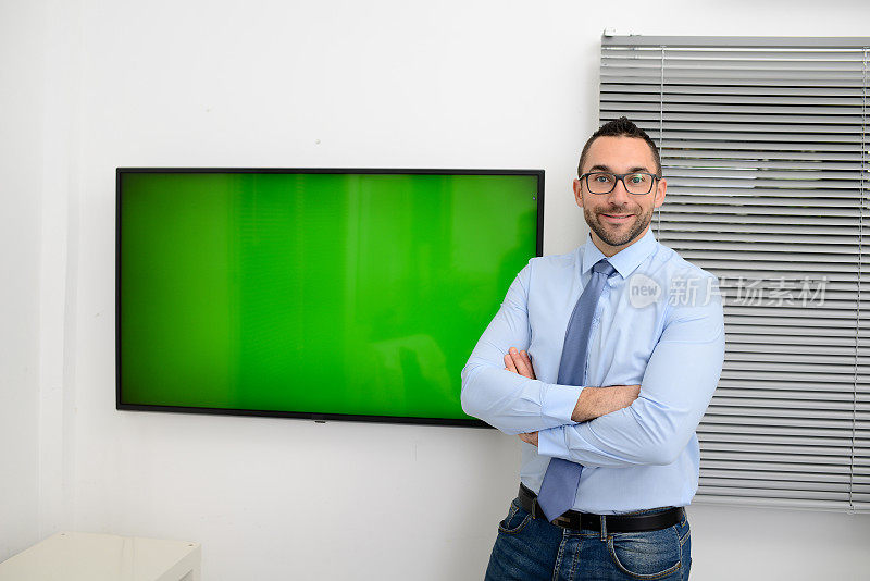 英俊年轻快乐的商人在休闲装商务展示会上站在电视屏幕前，展示绿色的色彩