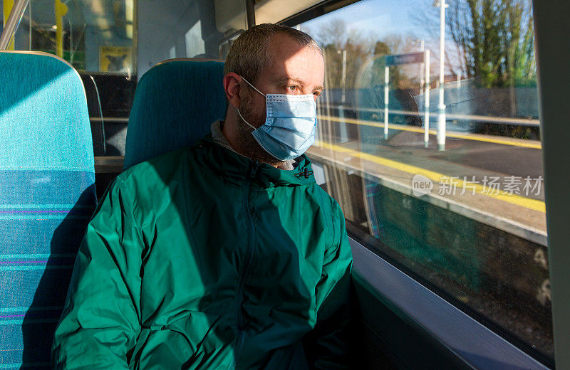 戴着防护面罩的男子望着火车窗外