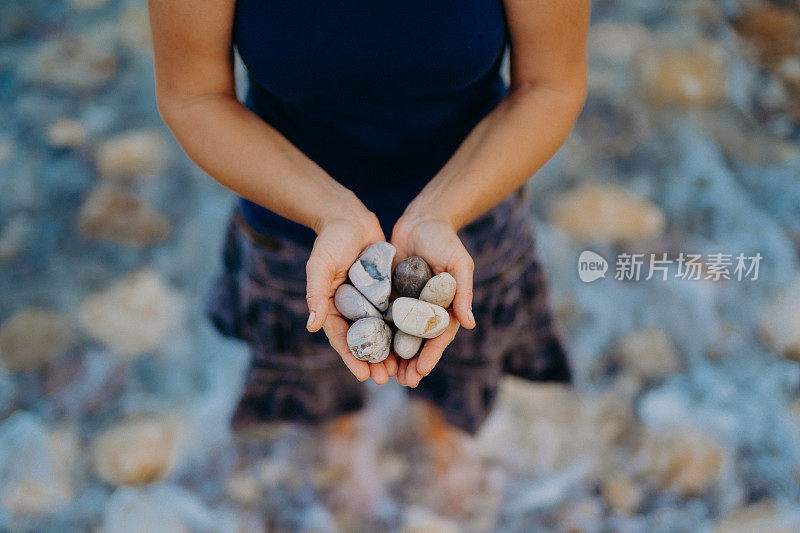 一个面目人非的女人手里拿着沙滩上的鹅卵石站在地中海海滩上的水里