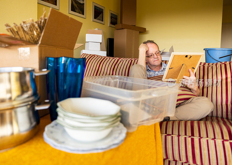 一个活跃的老人独自坐在沙发上，为搬家或公寓打开纸箱