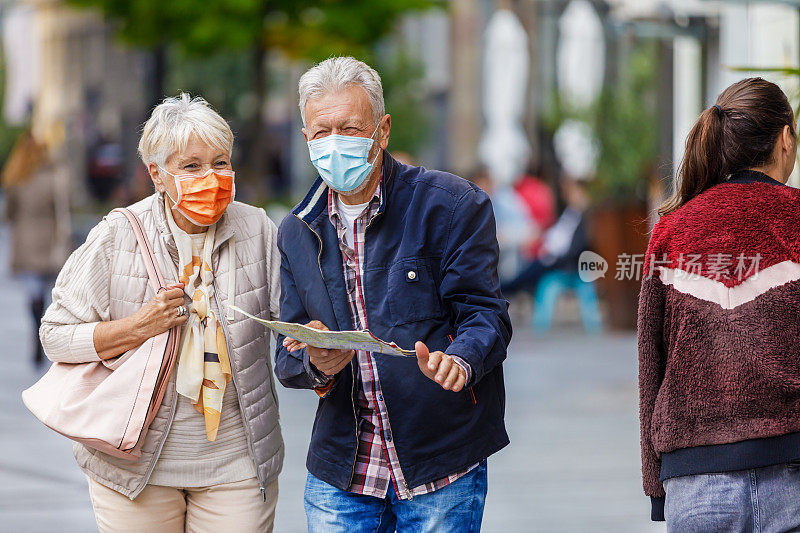 老人和他的妻子带着旅游地图，在流感大流行期间享受在市区散步。