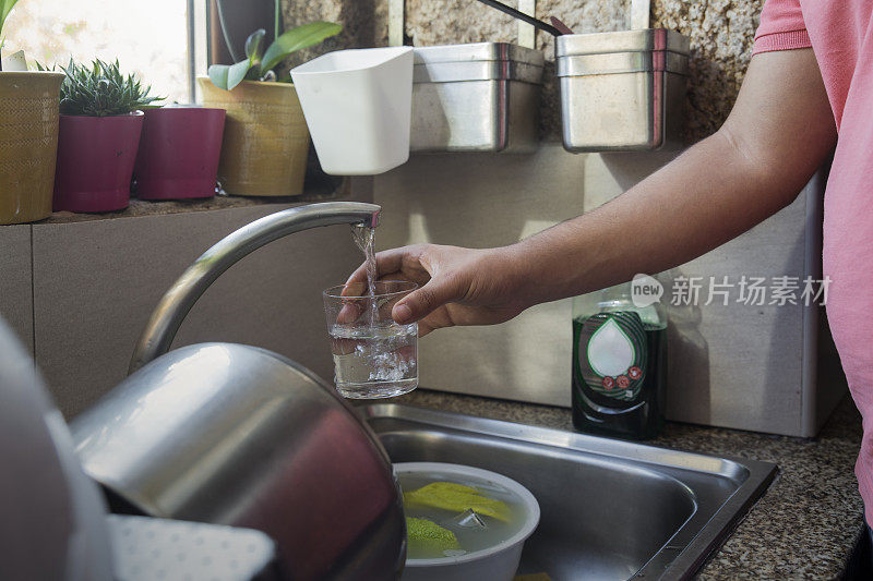 一个十几岁的女孩的手臂，正从厨房的水龙头里倒一杯水。