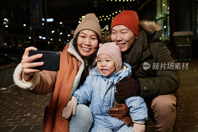 冬夜，亚洲女性与丈夫和孩子用智能手机拍摄的自拍照片