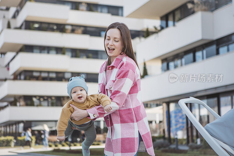 年轻的妈妈抱着婴儿，推着现代的婴儿车，漫步在城市中