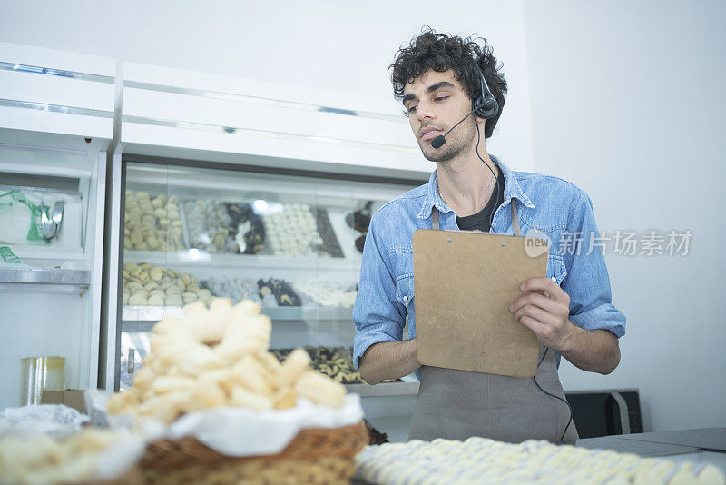 年轻的面包店员工戴着耳机，用写字板检查产品