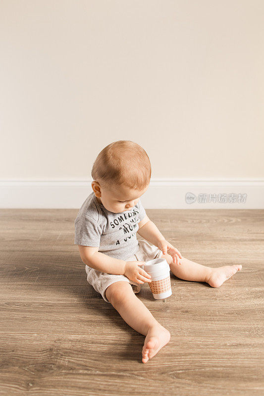 有12个脚趾的8个月大的流行病男婴穿着一件灰色的紧身衣，上面写着“谁给我妈妈拿杯咖啡!”一边玩咖啡杯牙签