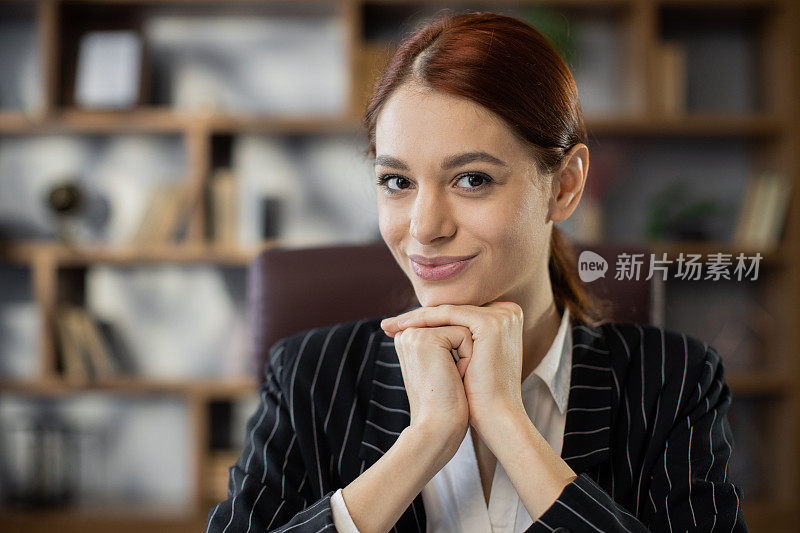 正面观点乐观有吸引力的年轻红头发妇女在正式服装坐在办公室的脸