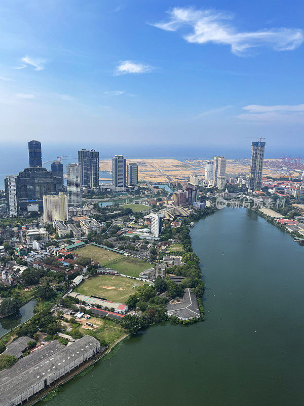 斯里兰卡科伦坡的城市景观图片，首都的摩天大楼，港口，道路，铁路轨道，港口起重机，蓝色多云的天空，重点在前景