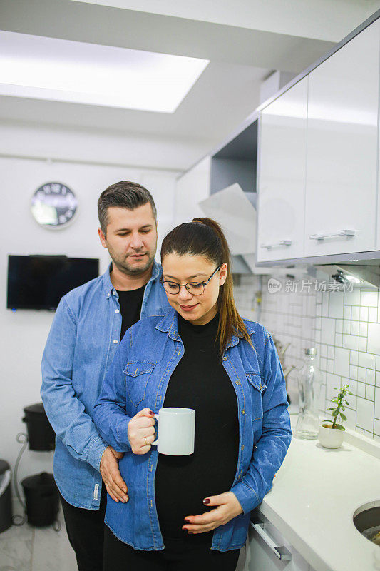 快乐的年轻孕妇和她的丈夫一起在厨房喝咖啡。新生的概念