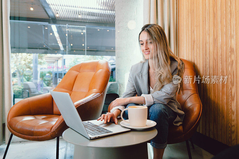 微笑的千禧商业女性工作，使用笔记本电脑，一杯咖啡在现代的工作场所。