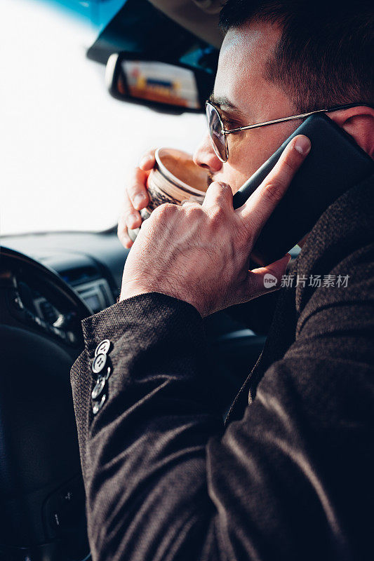 一名男子一边开车一边喝咖啡和玩手机