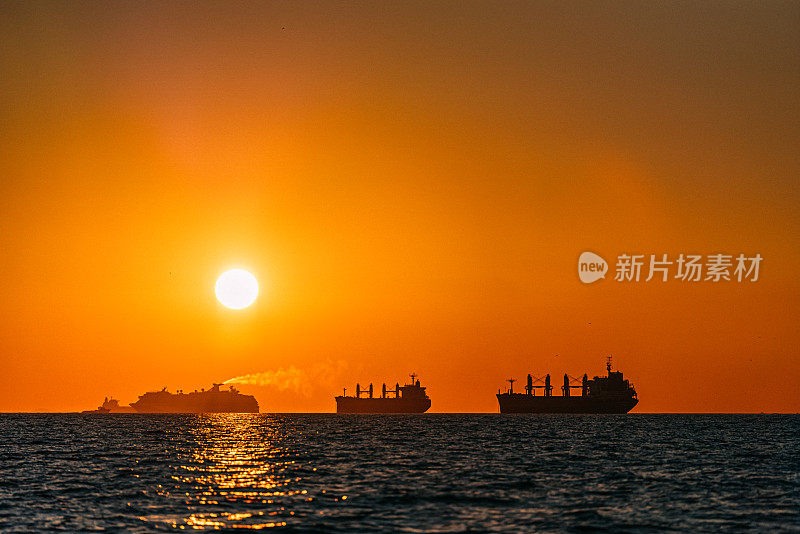 日落时分，两艘货船和一艘驶离的游轮的剪影在加利福尼亚州洛杉矶附近的亨廷顿海滩的太平洋上