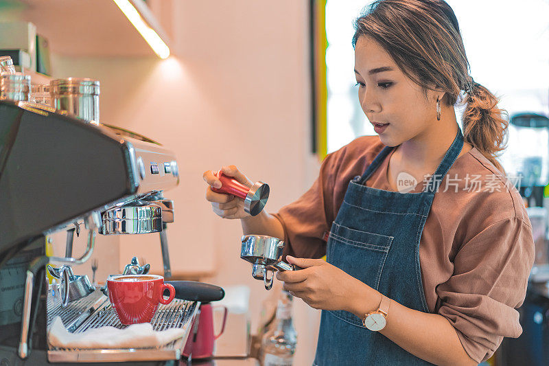 亚洲女咖啡师在咖啡店准备咖啡。