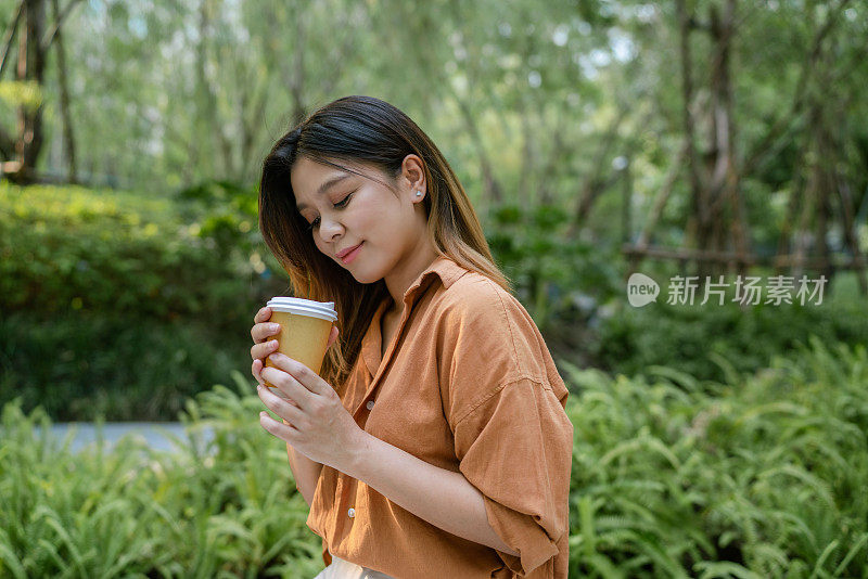 亚洲女人一边喝咖啡一边在城市花园享受简单的放松。