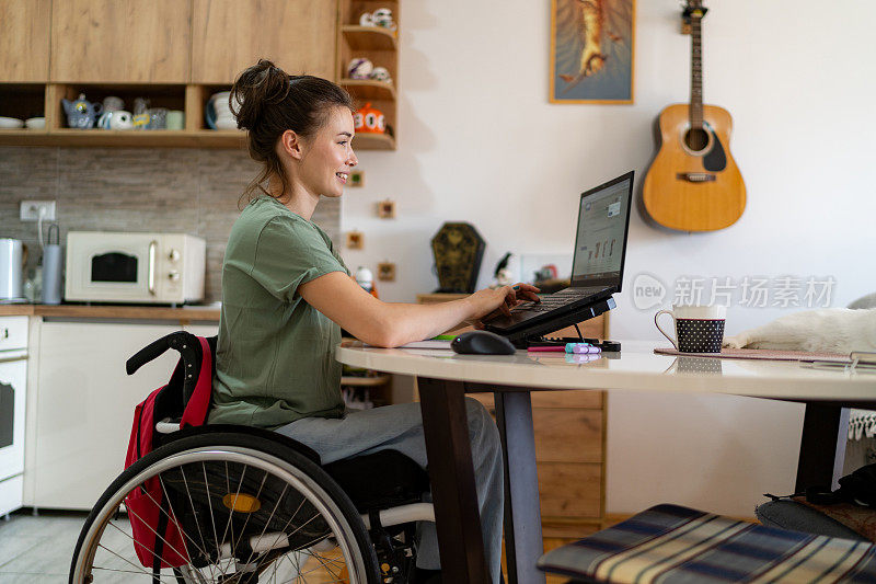 坐在轮椅上的快乐女人在家用笔记本电脑打电子邮件。