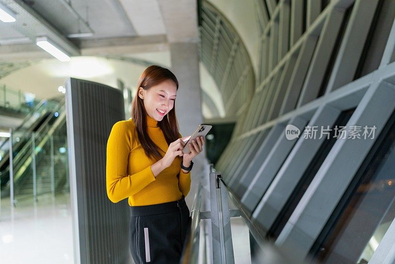 年轻的亚洲女子在机场候机厅候机时使用智能手机。出差的年轻女商人。生活方式和科技。年轻女子忙着做生意。随时随地的数字银行。