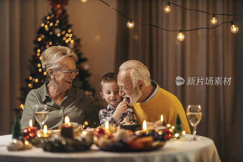 新年和平安夜，孙子和奶奶坐在家里，在圣诞餐桌上给爷爷喂饼干。