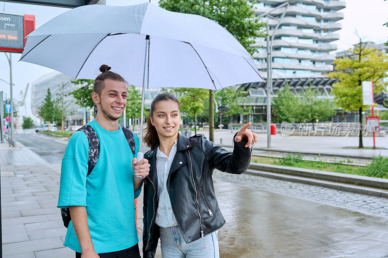 十几岁的男孩和女孩在公共汽车站撑着伞等公交车