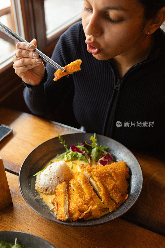 年轻女子在餐厅里吃着越南菜，配上蔬菜、鸡肉和咖喱酱米饭