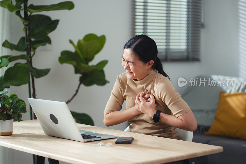 患有胸痛的亚洲女性坐在家里的办公室。