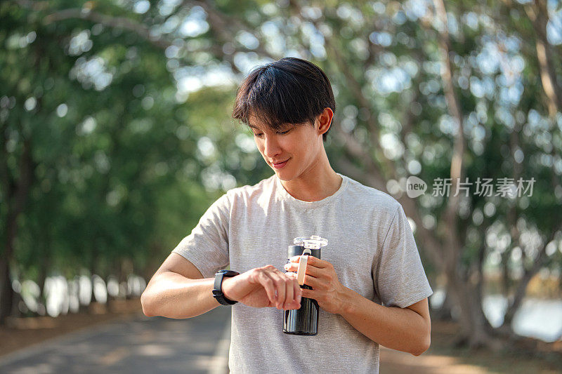 ชื่อผลงาน:快乐的亚洲人与smartwatch运动员检查他的运行时间,水瓶在公园户外。为了健康和健康而锻炼和训练。