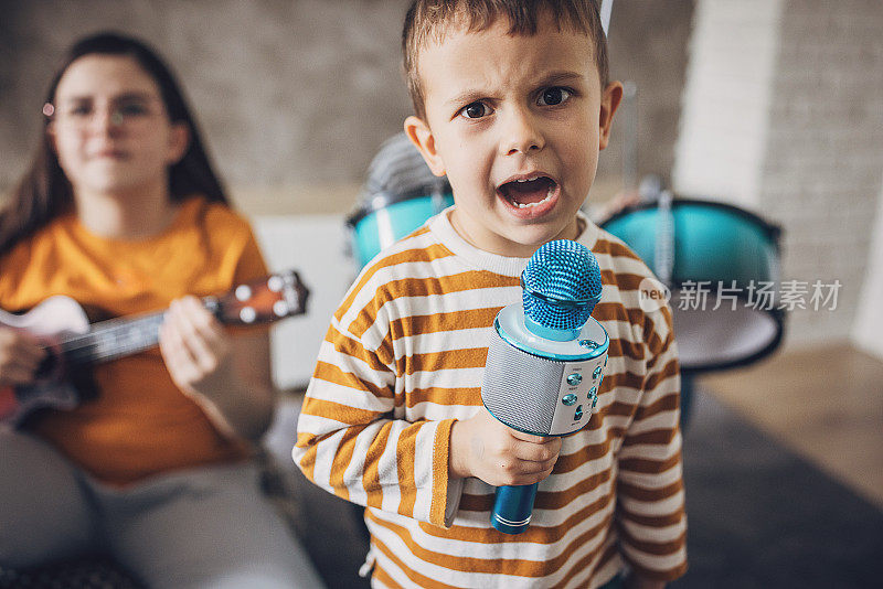 一个男孩对着麦克风唱歌，而其他孩子在弹奏乐器