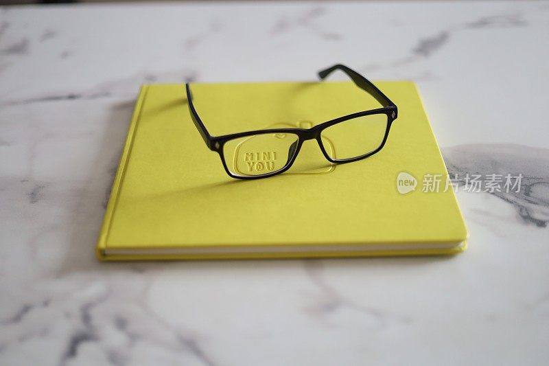 黄色的书和时尚的眼镜沐浴在柔和的光线下，唤起了文学魅力的场景。