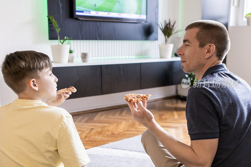 父子俩在一起玩得很开心。他们正在家里吃披萨，看他们最喜欢的足球队的电视转播。