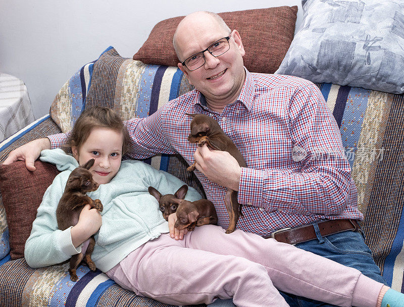 一个白人家庭，一个男人和一个8岁的女孩，开心地笑着，拥抱着布拉格大鼠犬的小狗。