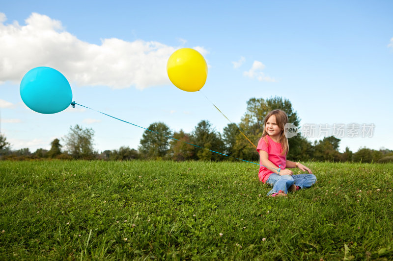 小女孩拿着气球，坐在草地上