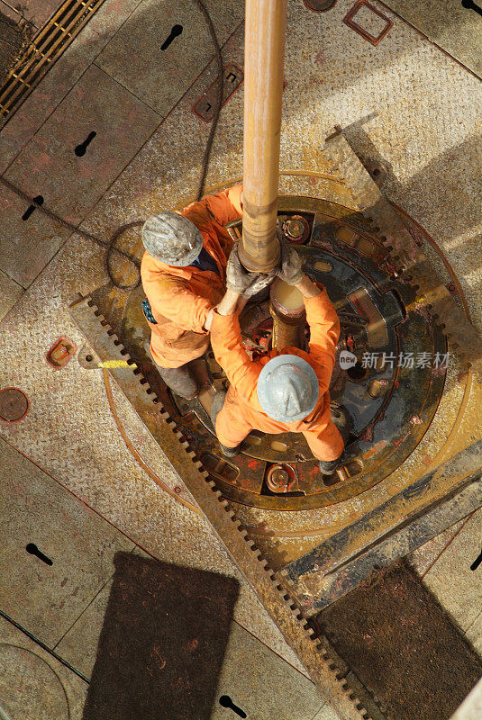 两个钻井操作员在一个石油钻塔上工作。