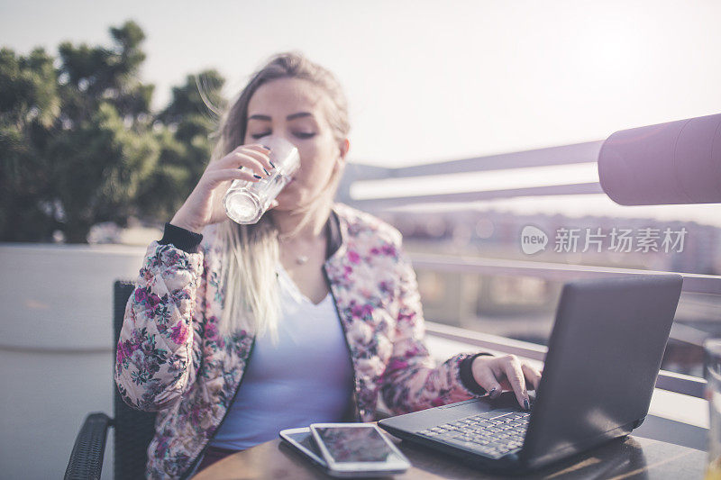 一位年轻的女商人坐在郊外的咖啡馆里用着笔记本电脑。