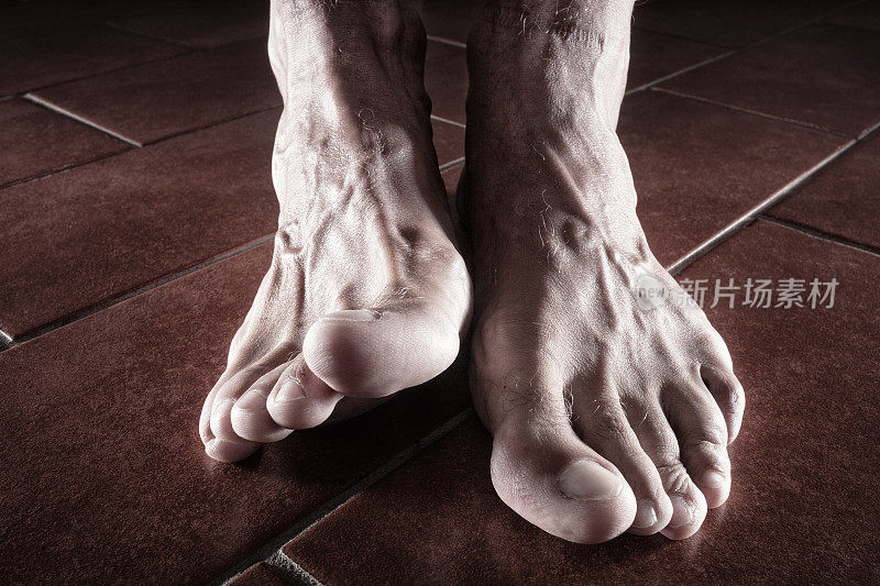 男性赤裸的脚在瓷砖地板上的特写