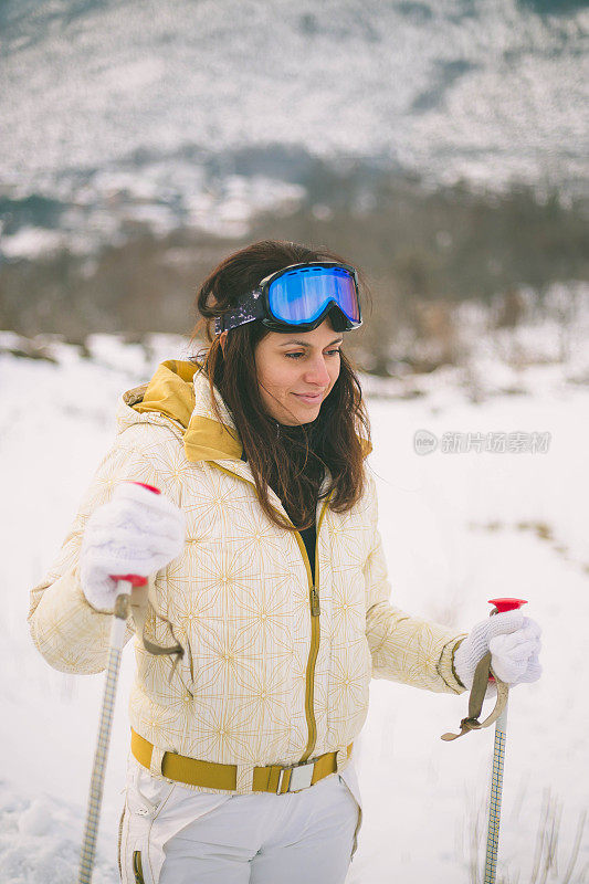 近景美丽的年轻女子在冬天的衣服站在一边，手拿木棍的背景雪山