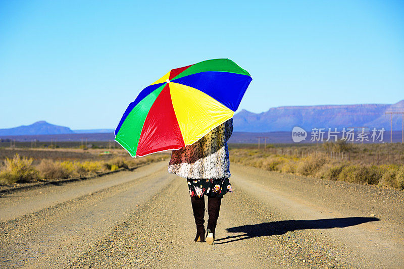 在沙漠中，一个女人打着伞走在碎石路上