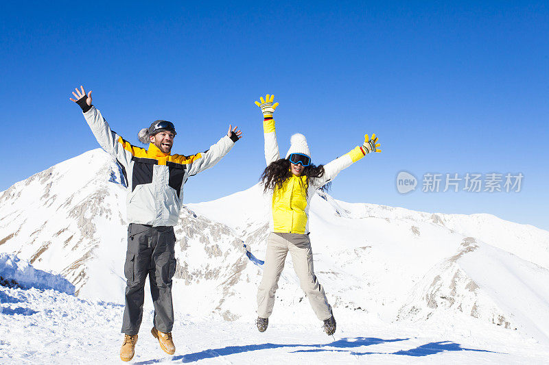 年轻的夫妇有乐趣和跳跃在山顶雪山