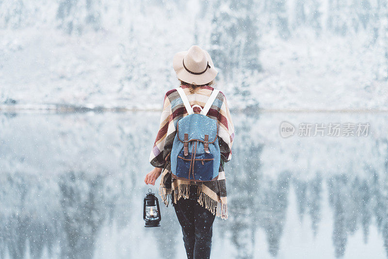 女旅人拿着煤油灯在雪湖边欣赏风景