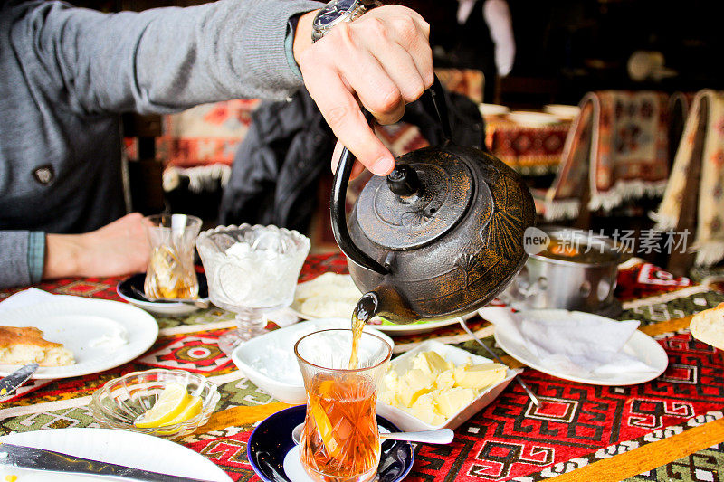 一个男人的手从金属壶里倒茶。巴库氛围和东方传统。东方美食
