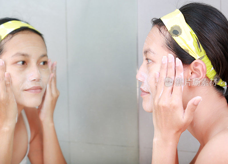 女人用浴室镜子在脸上涂抹泡沫霜。