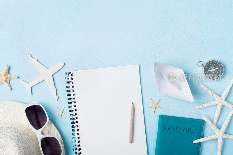 计划暑假和旅行的复古背景。带旅游配件的旅客笔记本在蓝色书桌上俯视图。