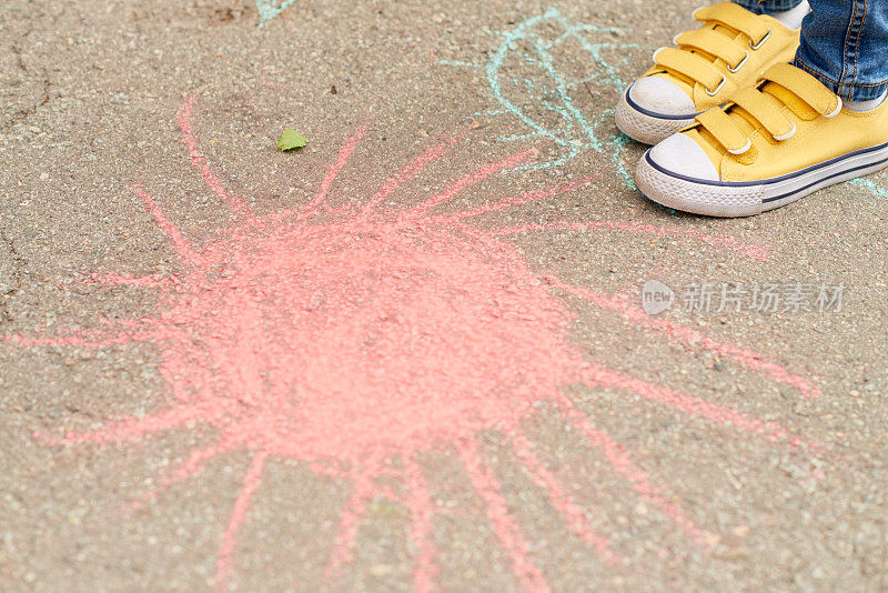双脚难以辨认的小女孩在黄色帆布鞋站在沥青旁边的红日粉笔画