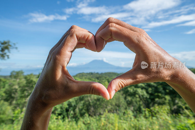 印尼巴厘岛阿贡火山上，双手制作心形手指架。人们旅行热爱自然的概念