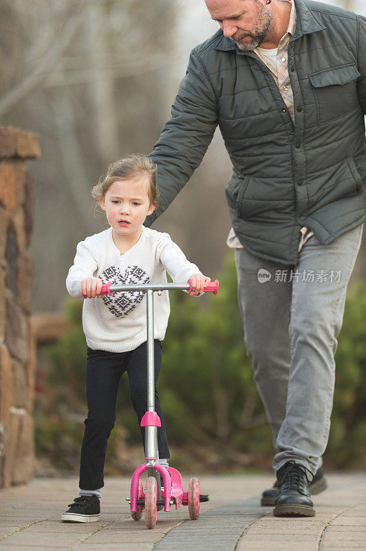 爸爸在帮他上幼儿园的女儿学骑滑板车