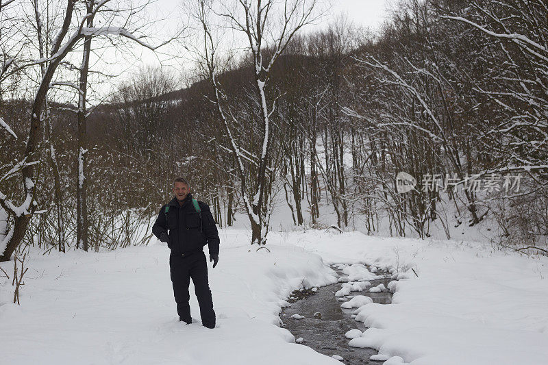 快乐的成年人徒步旅行在下雪的冬天大自然旁边流动的小溪在森林里
